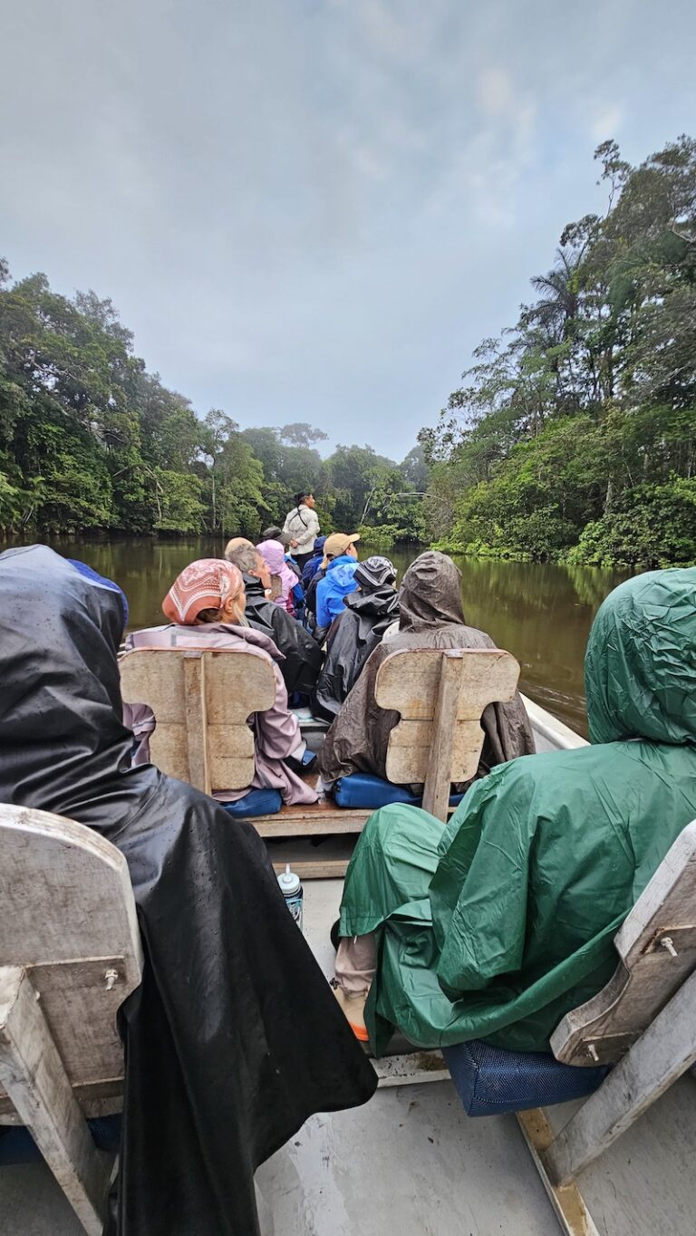 A group sits in a canoe, travelling on water through the Amazon rainforest.