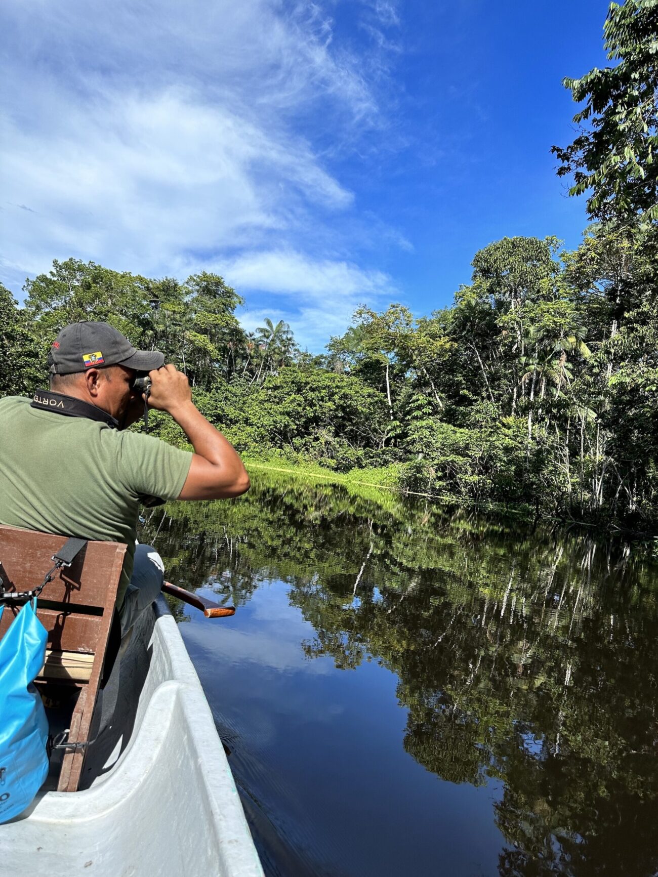 A man looks out on the water with binoculars on a boat in the Amazon rainforest.